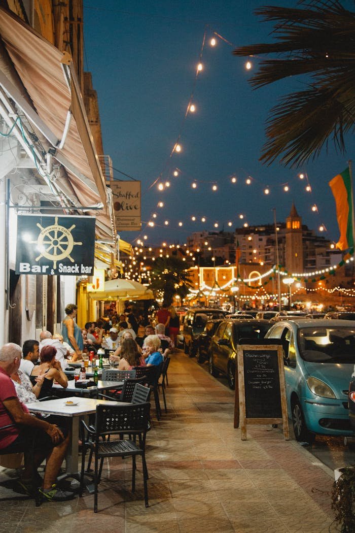 Bar Cafetería en Montanejos. A lively street scene in Mgarr, Malta, showcasing diners enjoying an evening at a bar with string lights.