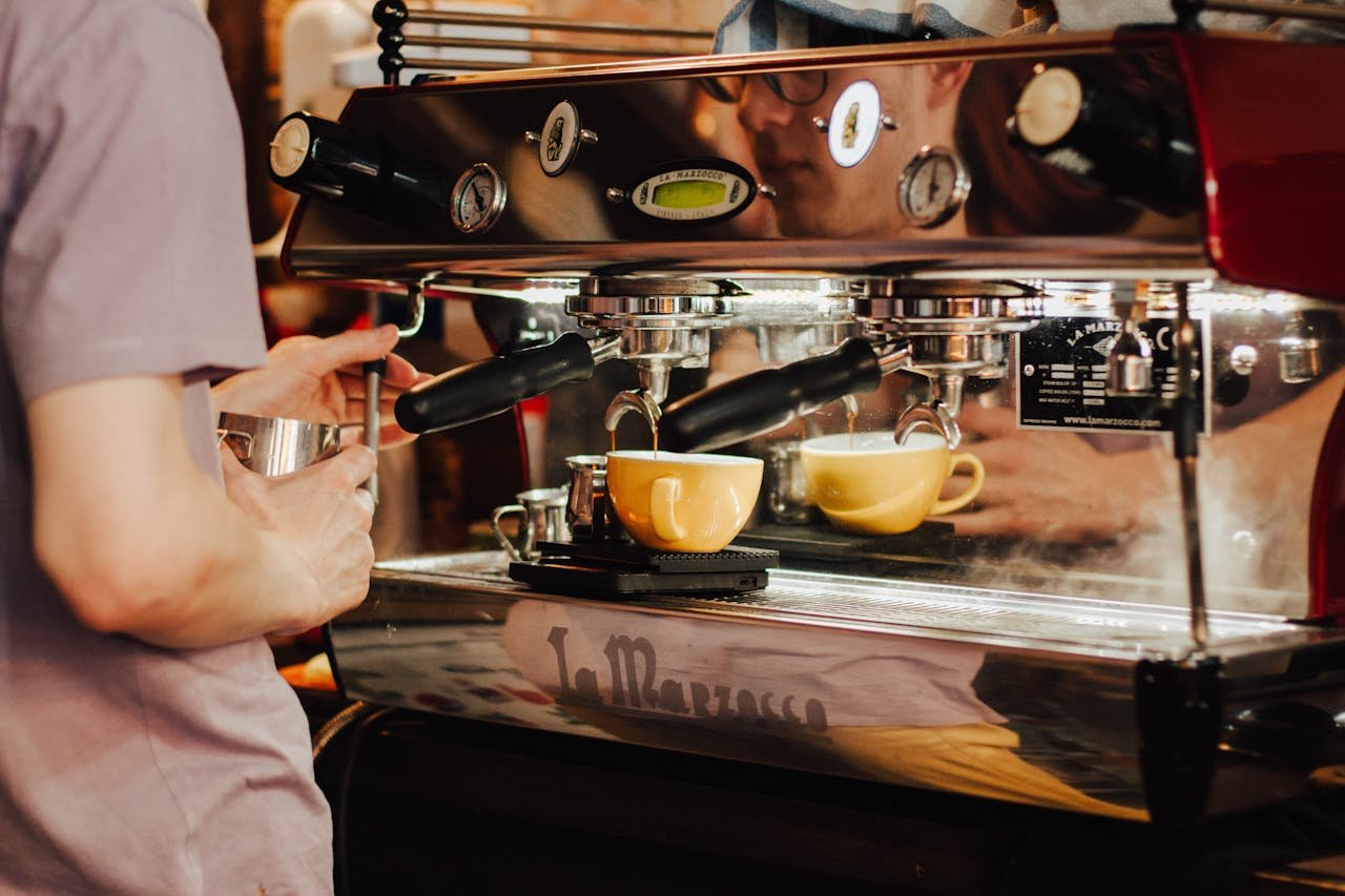 Bar Cafetería en Montanejos. Barista using espresso machine to brew coffee in a café, showcasing coffee preparation process.
